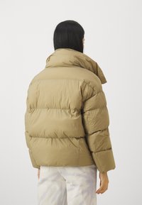 Pufferjacka i ljusbrunt med hög krage, quiltad design och oversized silhuett, matchad med ljusa jeans.