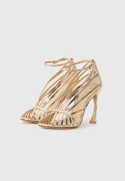 Gold open-toe high heels with multiple thin straps, a stiletto heel, and a smooth metallic finish. Features ankle strap with a buckle.