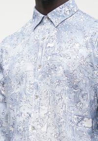 Šviesiai mėlyna marškiniai su sagomis, puošta gėlių ir abstrakčiu raštu, pagaminta iš austos medžiagos su tekstūruotu paviršiumi ir klasikinio kirpimo apykakle.