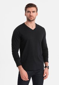 T-shirt nera a maniche lunghe con scollo a V, realizzata in tessuto misto cotone. Presenta una vestibilità slim e una texture liscia, abbinata a jeans scuri e un orologio.