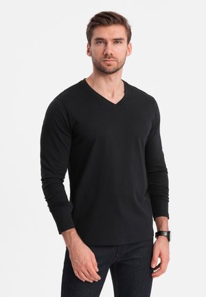 T-shirt noir à manches longues en V en tissu mélangé de coton. Présente une coupe slim et une texture lisse, associé à un jean foncé et une montre.