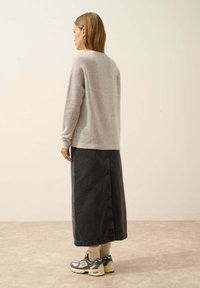 Grauer gerippter Pullover und schwarze Denim-Midikleid. Das Model trägt hellgraue Sneakers. Glatte Textur mit entspanntem Schnitt.