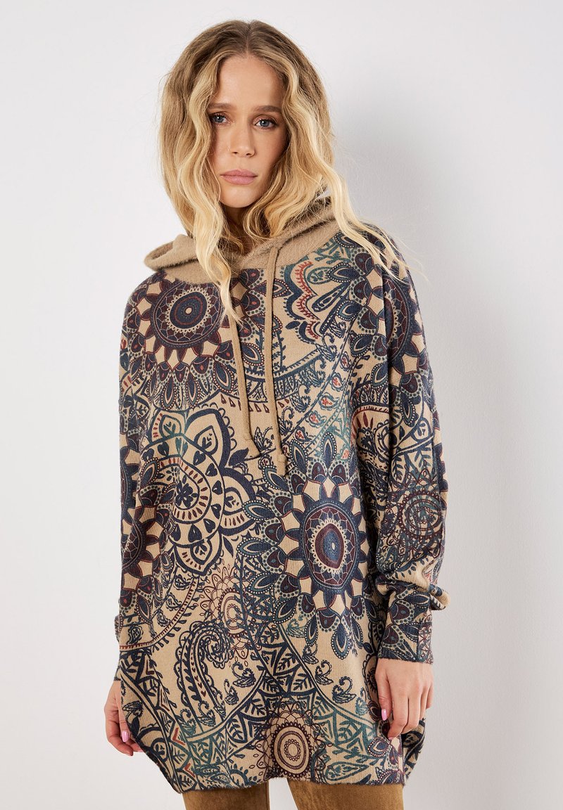 Sudadera con capucha que presenta una base beige con intrincados patrones azules y marrones, mangas largas y un ajuste relajado. Textura de tela suave.