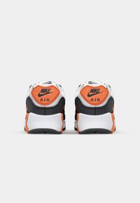 Crno-bijele Nike Air tenisice s narančastim akcentima, s teksturiranom potplatom, podstavljenim ovratnikom i istaknutim logotipima brenda na peti.
