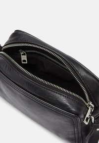 Schwarzlederne Crossbody-Tasche mit strukturierter Oberfläche, ausgestattet mit doppelten silbernen Reißverschlüssen und einem geräumigen Innenraum mit Stofffutter.