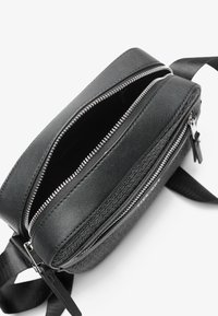 Sac bandoulière noir en cuir texturé, avec des fermetures éclair et des sangles en argent. Deux compartiments et finition lisse.