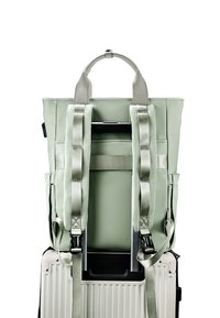 Zaino verde chiaro con spallacci regolabili, materiale sintetico, forma piatta e maniglia superiore, progettato per adattarsi al manico di una valigia.