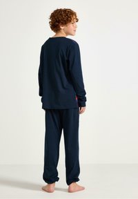 Ensemble de pyjama en coton bleu marine avec des manches longues et un pantalon ample. Présente un design simple avec un petit graphique coloré au niveau de l'ourlet.