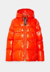Błyszcząca kurtka puchowa w jaskrawym pomarańczowym kolorze, z kapturem, zamkiem błyskawicznym z przodu i czarną metką marki. Wypełnione sekcje nadają efekt pikowania.