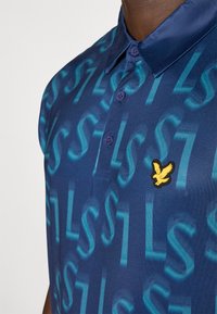 Navy polo shirt with a patterned design featuring large light blue letters. It has a button placket and a yellow embroidered eagle emblem.