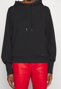 Sweat à capuche noir en matière douce avec une coupe ample, doté d'une capuche à cordon, de poignets côtelés et d'un petit logo sur l'ourlet.