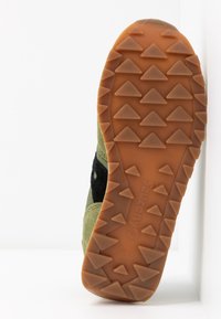 Vihreät mokkanahkakengät mustilla yksityiskohdilla, joissa on teksturoitu kumipohja, jossa on kolmionmuotoisia uria ja 'Saucony' -brändäys.