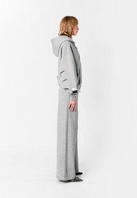 Sudadera gris con capucha y pantalones de chándal en un corte relajado, que cuentan con una capucha, detalles con aberturas en las mangas y piernas largas y sueltas con costuras laterales.