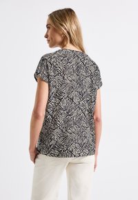 Top a maniche corte in nero e crema con un motivo a stampa zebra. Presenta una vestibilità comoda e un tessuto morbido e testurizzato.