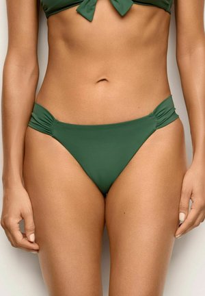 Kobieta nosząca zielone doły bikini ze ściąganymi bokami i pasujący top bikini zawiązany z przodu, widoczna od talii do górnej części ud.