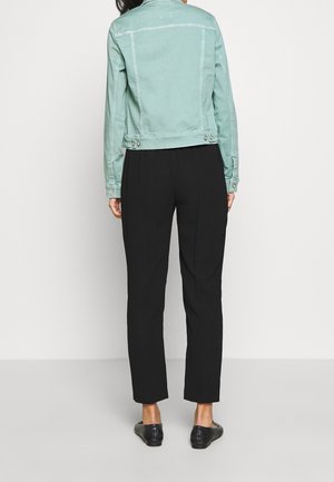 Personne portant une veste courte vert menthe, un pantalon droit noir et des mocassins noirs, debout dos à la caméra.