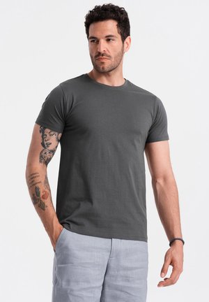 Camiseta de manga corta en gris oscuro, confeccionada en un tejido suave, con escote redondo y corte relajado. Se lleva con pantalones cortos de color claro.