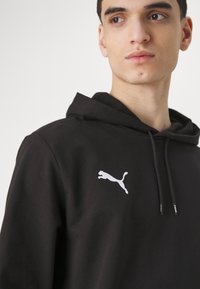 Zwarte hoodie van een katoenmengsel, met een voorste kangoeroezak en een wit Puma-logo op de linkerborst. Trekschoenen voor de capuchon.