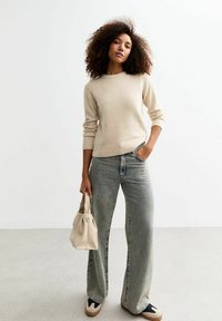 Pull beige à col rond, associé à un jean décontract�é à jambes larges en denim clair. Tenant un petit sac à main structuré beige.