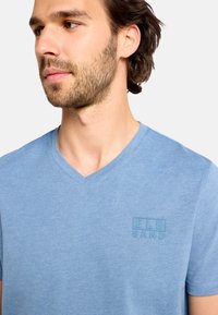 Svetlomodré tričko s výstrihom do V vyrobené z mäkkej látky, na hrudi s jemným vystúpeným logom. Krátke rukávy a voľný strih.