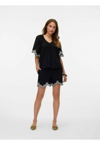 Zwart set met korte mouwen en shorts, met gegolfde zoom en witte geborduurde accenten. De stof lijkt lichtgewicht en zacht te zijn.