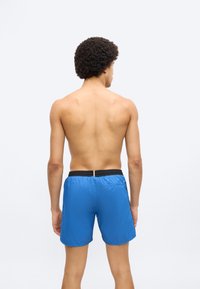 Μπλε μαγιό σορτς με μαύρη ελαστική μέση, πίσω τσέπη και ελαφρύ υλικό. Σχεδιασμένο για άνεση και ευκολία στην κίνηση.