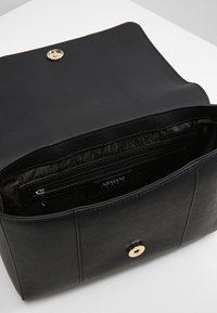 Borsa a tracolla in pelle nera con textura, chiusura a pulsante dorato, aperta per mostrare la tasca con zip interna e l'etichetta Armani Jeans all'interno.