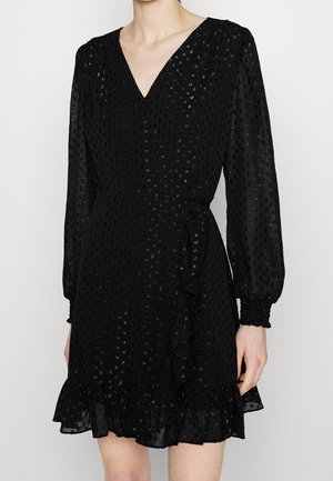 Schwarzes Wickelkleid mit strukturierten Punkten, V-Ausschnitt, langen Ärmel mit gerafften Bündchen und einem Rüschensaum. Hergestellt aus leichtem Stoff.