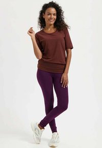 Bruin shirt met korte mouwen in combinatie met paarse leggings, met een aansluitend ontwerp. De outfit wordt compleet gemaakt met witte sportieve sneakers.