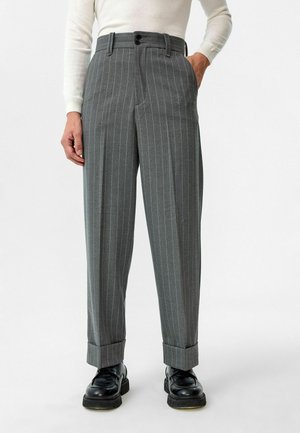 Grijze gestreepte broek met een losse pasvorm, voorzien van een dubbele knoopsluiting, riemlussen en opgerolde manchetten, gecombineerd met zwarte schoenen.