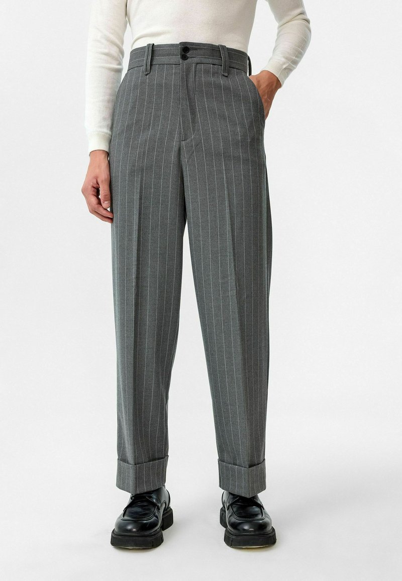 Grijze gestreepte broek met een losse pasvorm, voorzien van een dubbele knoopsluiting, riemlussen en opgerolde manchetten, gecombineerd met zwarte schoenen.