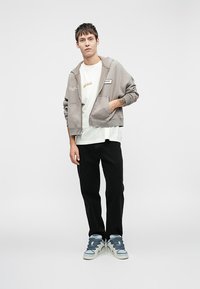 Hallidega hall kapuutsiga soe särk, millel on küljetaskud, valge T-särk all, mustad püksid ja sinised tossud kihilise paelaotsaga. Lihtne disain ning mugav lõige.