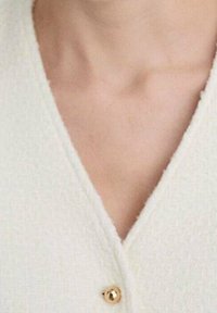 White textured cardigan featuring a V-neck design and a gold button closure at the neckline, highlighting clean lines and soft fabric.