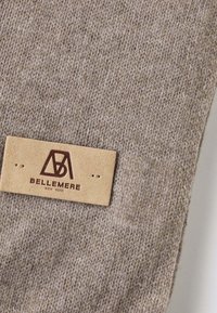 Tessuto lavorato a maglia beige con una texture morbida, caratterizzato da un'etichetta rettangolare in pelle color tabacco impresso con "BELLEMERE NEW YORK."