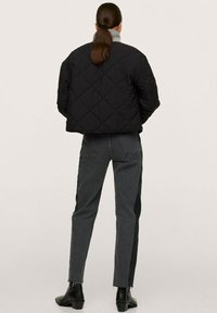 Veste matelassée noire avec un design court et un motif en losanges, associée à un jean gris foncé avec des accents latéraux.