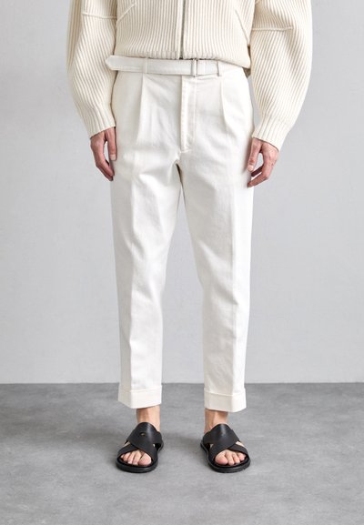 Weiße Baumwollhosen mit gefaltetem Front, kürzerer Länge und umgeschlagenem Saum, kombiniert mit schwarzen Sandalen mit Kreuzriemen. Strukturierter cremiger Pullover.