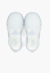 Valged, läbipaistvad plastist sandaalid, millel on ruuduline disain, suletud varbad ja reguleeritavad tagarihmad. Logo "igor" on nähtav sisetalladel.