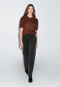 Bruine, textuurgegeven polo met korte mouwen gecombineerd met hooggeritste zwarte corduroybroek en zwarte enkellaarsjes. Eenvoudig, aansluitend ontwerp.