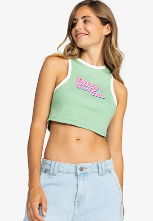 Zeleni crop top s bijelim rubom i ružičastim natpisom "ROXY Surf Club". Izrađen od pamuka s pripijenim dizajnom. Uparen s svijetloplavim trapericama.