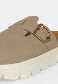 Μπεζ παπούτσι τύπου slip-on με παχιά λευκή ραβδωτή σόλα και ρυθμιζόμενο χρυσό αγκράφα στο επάνω λουράκι.