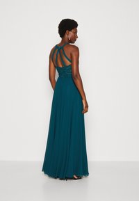 Rochie de seară verde-albăstrui cu un corsaj intricately brodat și o spate decupat, având o fustă fluidă dintr-un material ușor.