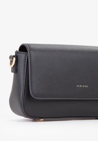 Sort tekstureret læder skuldertaske med klaplukning, guldfarvet hardware og præget brandlogo på fronten.