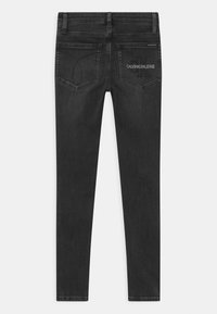 Jeans skinny de algodón negro con una textura suave, que cuentan con dos bolsillos traseros y un bordado con la marca "CALVIN KLEIN JEANS" en el bolsillo derecho.