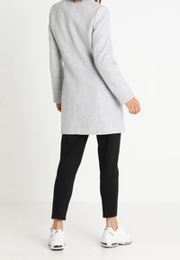 Cappotto in misto lana grigio con una vestibilità strutturata e maniche lunghe, abbinato a pantaloni neri slim e sneakers bianche, visto da dietro.