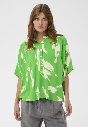 Zelená košeľa s bielymi abstraktnými vzormi štetca, golierový strih a zapínanie na gombíky vpredu. Krátke rukávy, voľný strih a mäkká textúra látky.