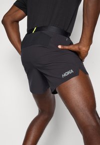 Black running shorts made of lightweight fabric, featuring a breathable design, a rear pocket, and a reflective logo on the leg.
