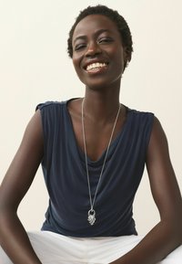 Navy blouse met korte mouwen, gecombineerd met witte broeken. Zilveren ketting met een hanger in een ingewikkeld bladmotief.