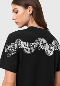 Maglietta nera in cotone con una grafica di serpente prominente e testo stilizzato sul retro. Maniche corte e design a girocollo.
