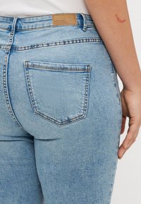 Jeans de denim azul claro com uma cintura alta, apresentando detalhes de costura, uma etiqueta da marca na parte de trás e um design de bolso traseiro único.
