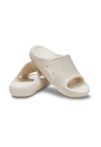 Beżowe buty slip-on z żebrowaną powierzchnią, otwartym palcem i zaokrąglonymi krawędziami. Wykonane z lekkiego materiału o gładkiej teksturze.